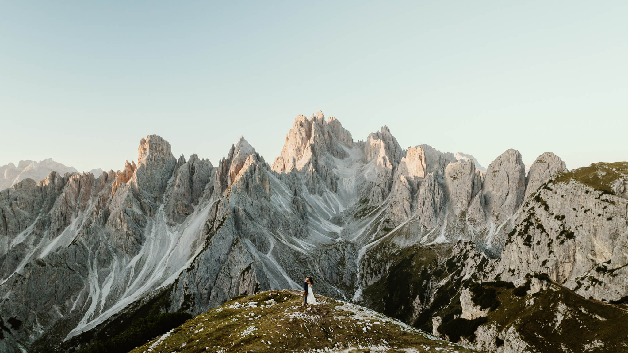 man and woman standing on a hill at the italian dolomites in wedding attire.