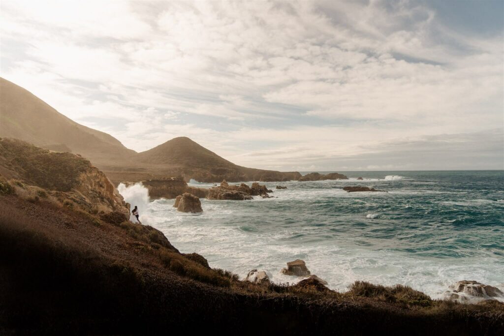 a man and woman standing on the a cliff on the california coast of Big Sur.